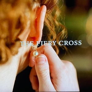 May include: A close-up of a woman's ear with a pearl earring. The text "THE FIERY CROSS" is visible in the background.