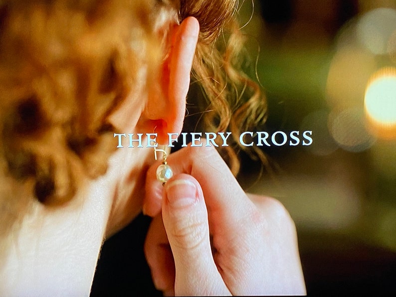 May include: A close-up of a woman's ear with a pearl earring. The text "THE FIERY CROSS" is visible in the background.