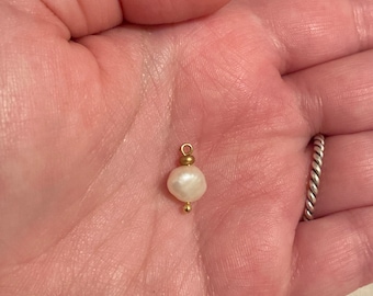 May include: A white pearl pendant with a gold bail and a small gold bead at the bottom.