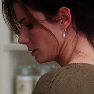 May include: A woman with dark brown hair wearing a brown sweater and a pearl earring. She is looking down and appears to be in a shop.