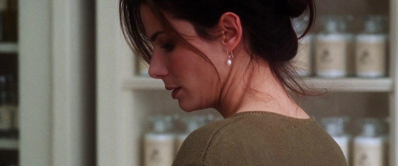 May include: A woman with dark brown hair wearing a brown sweater and a pearl earring. She is looking down and appears to be in a shop.