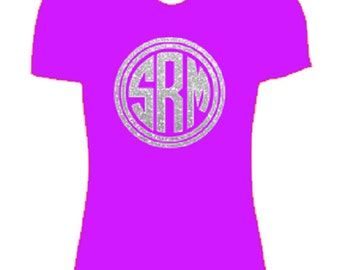 May include: A bright purple t-shirt with a silver glitter circle monogram that says "SKM".