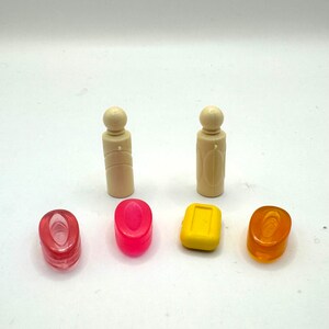 May include: Five small items, including two white plastic bottles, two pink soap bars, and one yellow soap bar. The items are arranged in a row on a white surface.