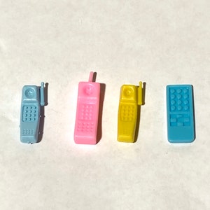 May include: Four miniature toy phones in different colors: blue, pink, yellow, and light blue. The phones have a retro design with buttons and a small antenna.