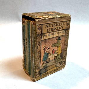 May include: A vintage Nutshell Library book set by Maurice Sendak housed in a tan cardboard slipcase. The front features an illustration of a child and a crocodile at a table, with the text Nutshell Library by Maurice Sendak and Harper & Row.
