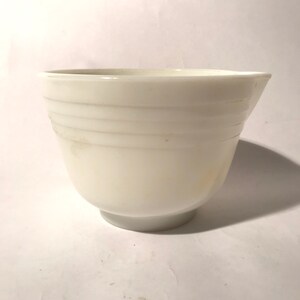 May include: White ceramic mixing bowl with a rounded bottom and a pouring spout. The bowl has a smooth, glossy finish and features three horizontal lines around the exterior.