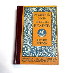 May include: A vintage copy of McGuffey's Sixth Eclectic Reader, Revised Edition. The book has a maroon spine and a cover with an orange center panel featuring the title and a ship illustration. The cover is framed with blue and white floral designs.