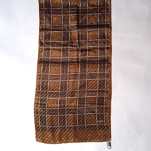 May include: A brown silk scarf with a plaid pattern in shades of brown, pink, and white. The scarf has a fringed edge.