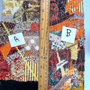 May include: A close-up of a fabric patchwork quilt with a variety of colors and patterns, including orange, brown, and gold. The quilt is stitched together with a spiderweb design and includes the word "Halloween". The quilt is labeled with the letters "A" and "B".