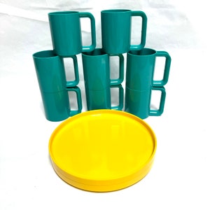 May include: A set of six green plastic mugs stacked on top of each other. A yellow plastic tray is in front of the mugs.