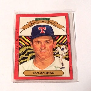 May include: A red baseball card with a white border featuring Nolan Ryan, a baseball player for the Texas Rangers. The card is from the Donruss King of Kings series. The card features a portrait of Nolan Ryan in his baseball uniform with a Texas Rangers cap. The card also features a smaller image of Nolan Ryan pitching.