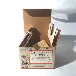 May include: A brown cardboard box with a white interior. The box is open and contains a timer. The box is labeled "AMF PARAGON MODEL APT15-0 HEAVY-DUTY 24 HR. TIMER CAPACITY 15 AMPS 1800 W. 1/4 H.P. 120 VOLTS 60 CYCLES IN CANADA, PARAGON ELECTRIC Division of AMF CANADA, UNITED Don Mills Ontario"