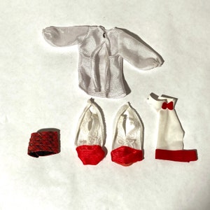 May include: A set of doll clothes including a white lace top, a white shirt with red trim, a red and black plaid skirt, and a pair of white lace shoes with red trim.