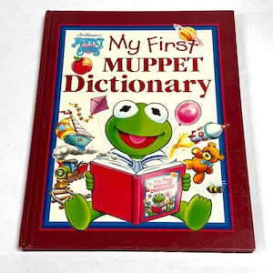 May include: A hardcover children's book titled "My First Muppet Dictionary" featuring Kermit the Frog reading a book. The cover is red with a blue border and illustrations of various Muppet characters and objects.