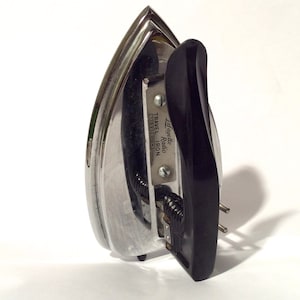 May include: A silver travel iron with a black handle. The iron has the text "Lafayette Radio TRAVEL IRON 110V 250W" printed on the side.