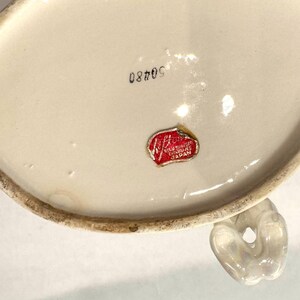 May include: Off-white ceramic piece with a handle. The bottom of the piece has the number "50480" printed in black ink. A red and white sticker with the text "Regus of Exclusives Japan" is affixed to the ceramic.