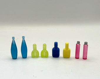 May include: A set of eight miniature glass bottles in various colors, including blue, yellow, and pink. The bottles are arranged in a row on a white surface.