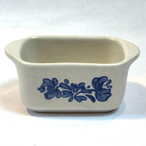 May include: A rectangular, off-white ceramic dish with rounded handles. The dish features a blue floral design on the front. The interior is a lighter shade of off-white. This vintage-style dish is suitable for serving or display.