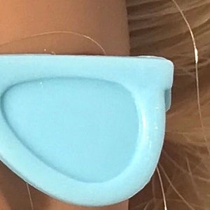 May include: A pair of light blue plastic sunglasses with a rounded, modern shape.