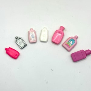 May include: A set of seven miniature plastic bottles in various colors, including pink, white, and gray. The bottles are all different shapes and sizes, and some have labels with text.