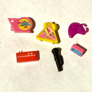 May include: A set of six colorful plastic toys, including a pink alarm clock with the word "Barbie" on it, a yellow triangle-shaped alarm clock, a purple video game controller, a red stereo, a black microphone, and a pink digital clock.