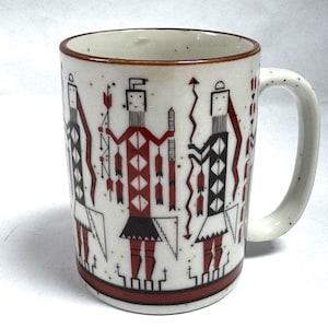 May include: A ceramic mug with a speckled off-white finish featuring a repeating pattern of stylized figures in black and red. The figures hold arrows and geometric shapes. The mug has a brown rim and a matching brown band around the base.