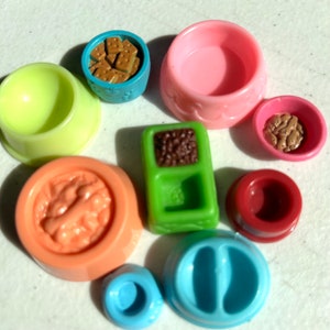 May include: A set of nine colorful plastic pet bowls, including a green bowl with two compartments, a pink bowl, a blue bowl, a yellow bowl, a red bowl, and three bowls with different designs. The bowls are perfect for feeding small pets.