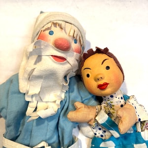 May include: A pair of vintage hand puppets, one depicting a blue-clad Santa Claus with a white beard and the other a girl with a floral dress and blue overalls.