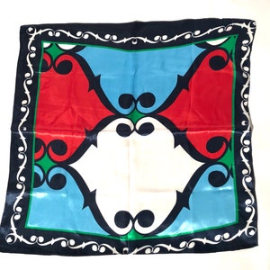 May include: A blue, red, white, and green patterned silk scarf with a black border. The pattern is geometric and features a repeating design of swirls and curves.