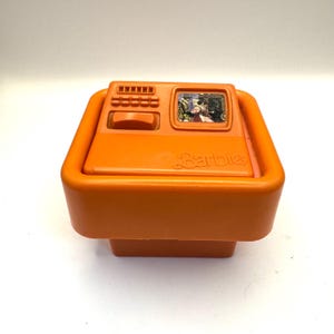 May include: Orange plastic toy television with a screen showing a cartoon image and the word "Barbie" on the front.