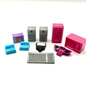 May include: A collection of miniature toy electronics, including a purple television with a bear graphic, two blue cash registers, gray speakers, a black camera flash, a gray keyboard, a pink speaker, a purple car seat, and a pink microwave.