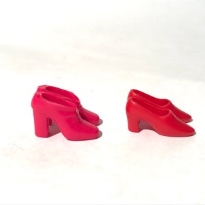 May include: Two pairs of red high-heeled shoes for a doll. One pair is a closed-toe style and the other pair is an open-toe style.
