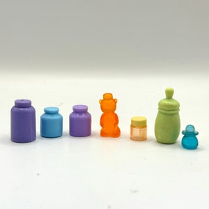 May include: A set of seven miniature bottles and a bear figurine. The bottles are in various colors, including purple, blue, green, and yellow. The bear is orange and has a hat. The bottles are all about 2 inches tall.