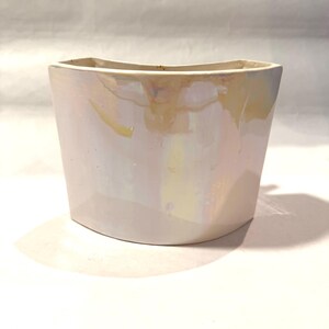 May include: A pearlescent white ceramic planter with a curved front and a rectangular top. The planter has a glossy finish with subtle iridescent hues of yellow and pink. The design is modern and minimalist, suitable for indoor plants.