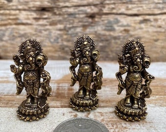 May include: Three small gold-colored statues of the Hindu deity Ganesha. Each statue is standing on a circular base with intricate details. The statues are made of metal and have a traditional design.