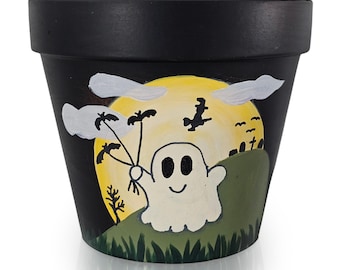 以下が含まれることがあります： ハロウィーンをテーマにした黒く塗られた植木鉢。 植木鉢には、黄色い月の前でコウモリを持っている笑顔の白い幽霊が描かれています。 背景には雲、魔女、墓地のシーンが含まれています。 屋内または屋外での使用に適しています。
