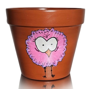 May include: A terracotta flower pot with a hand-painted pink bird with large eyes and purple accents. The bird has a long neck and long legs.