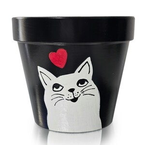 Peut inclure: Pot de fleur en céramique noire peint avec un visage de chat blanc et un cœur rouge. Le chat a une expression souriante. Convient pour une utilisation intérieure ou extérieure. Environ 15 cm de haut.