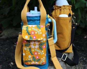 May include: Two water bottle carriers. The first is teal with a mustard yellow strap and a mustard yellow pocket with a floral design. The second is mustard yellow with a black strap. Both have a handle and a shoulder strap.