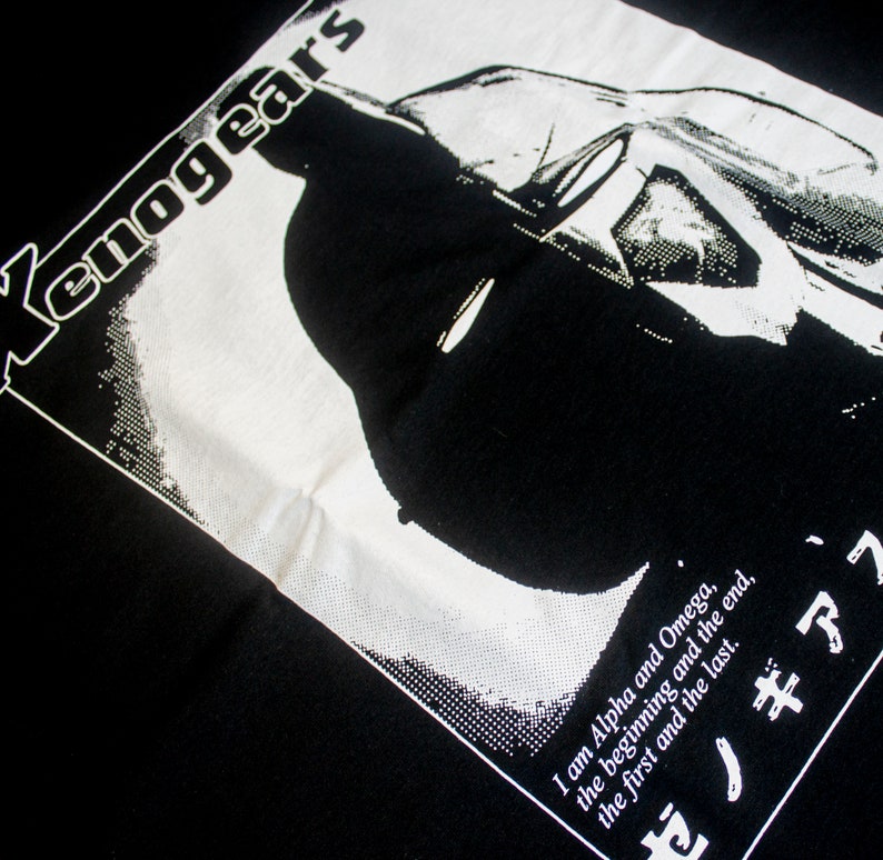 May include: Black and white graphic t-shirt with the text "Xenogears" and a silhouette of a character. The text below the character reads "I am Alpha and Omega, the beginning and the end, the first and the last. ゼノギアス"