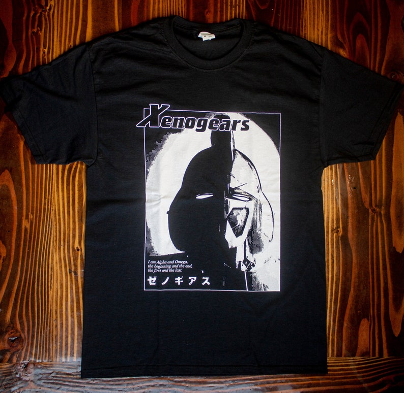 May include: Black t-shirt with a white graphic print of a helmet and the text "Xenogears" and "I am Alpha and Omega, the beginning and the end, the first and the last, ゼノギアス".