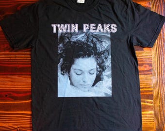 Może przedstawiać: Czarny T-shirt z białym nadrukiem graficznym twarzy kobiety i tekstem "Twin Peaks" nad obrazem.