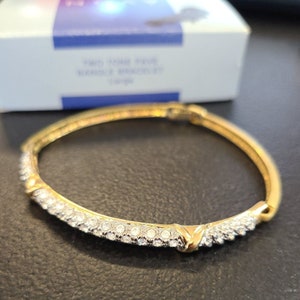 May include: A gold bangle bracelet with a row of clear rhinestones around the edge.