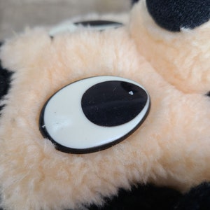May include: Close-up of a plush toy's eye. The eye is a black circle with a white oval around it. The eye is sewn onto a light peach-colored plush surface.