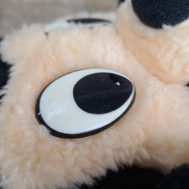 May include: Close-up of a plush toy's eye. The eye is a black circle with a white oval around it. The eye is sewn onto a light peach-colored plush surface.
