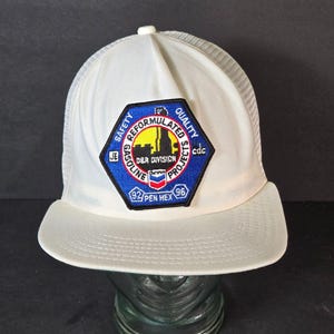 May include: White mesh trucker hat with a blue and yellow patch that says "Safety Reformulated Quality Projects D&R Division Gasoline 92/Pen Hex 96 cdc JE".
