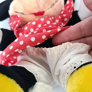Pu&ograve; includere: Un giocattolo di peluche nero e giallo vestito con un vestito a pois rossi e bianchi con un bordo di pizzo bianco. Il giocattolo ha un naso nero e labbra rosse.