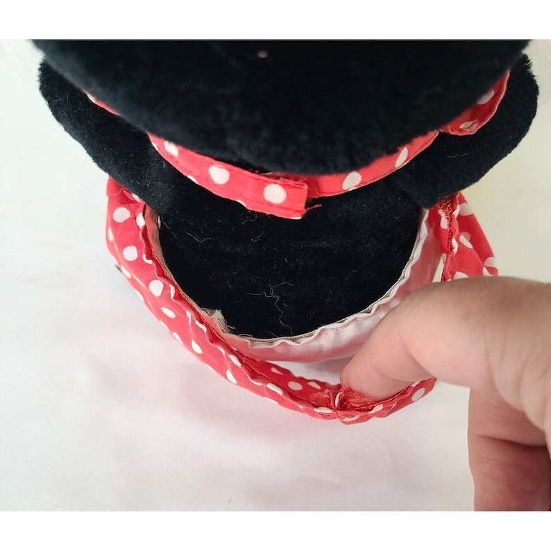 Pu&ograve; includere: Un giocattolo di peluche nero con una gonna a pois rossi e bianchi. Il giocattolo indossa un cappello nero e ha una fodera bianca intorno alla gonna.