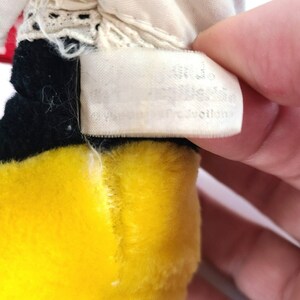 Pu&ograve; includere: Primo piano di un giocattolo di peluche giallo e nero con un'etichetta bianca che recita "100% Polyester Fiberfill", "Made in China" e "All New Material".