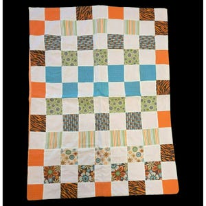 May include: A rectangular patchwork quilt featuring a grid of alternating white squares and patterned squares. The patterns include orange solids, brown tiger stripes, green floral prints, blue geometric textures, and multi-colored vertical stripes.